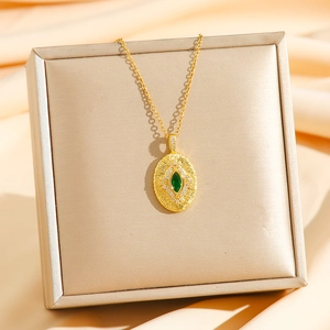 Pendentif ovale en zircon vert émeraude de luxe sur chaîne dorée et fond en soie champagne