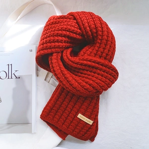 Thick red knit scarf with handmade leather label placed on white canvas bag and magazine