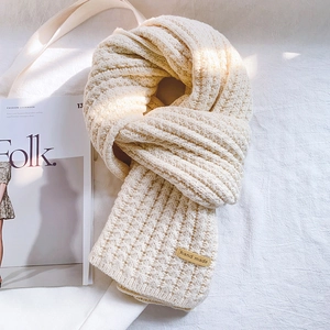 Detail of chunky knit scarf texture with a handmade leather tag on a soft fabric background