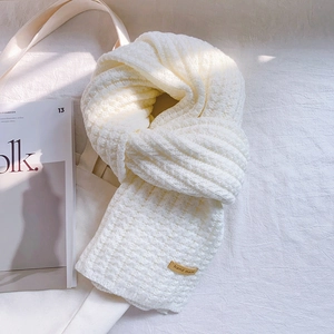 Thick beige knitted scarf with handmade leather label on a clean aesthetic background