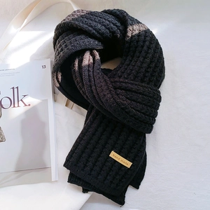 Close-up of black chunky knit scarf featuring a handmade leather label on soft fabric
