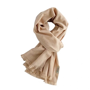 Solid light brown cashmere style scarf with soft fringe trim and brand tag on white background