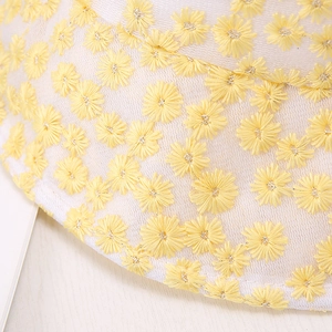 Détail de la broderie de marguerites jaunes sur un chapeau de soleil en maille blanche