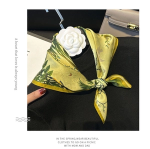 Detail of floral silk scarf in yellow and green tied on a black knit sweater