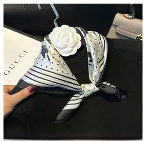 Detail of a silk scarf with black white polka dots and stripe pattern with camellia brooch