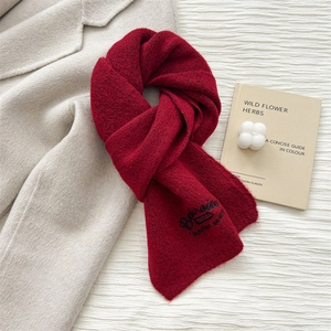 Detail of red knitted scarf with black embroidery on beige wool coat background