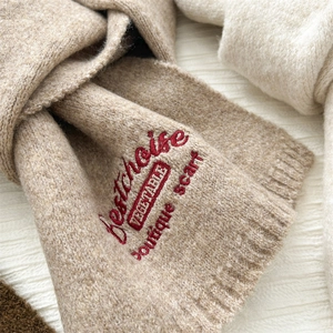 Detail of oatmeal knit scarf featuring red embroidered boutique scarf lettering
