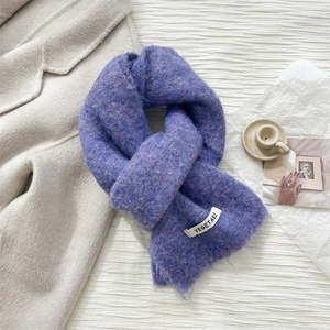 Detail of purple knit wool scarf with VEGETABLE fabric label on textured white surface