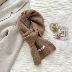 Detailed texture of brown wool knit scarf with white woven label on beige cashmere coat