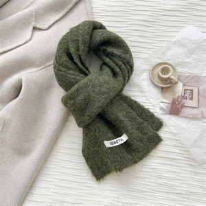 Detail of dark green knit wool scarf showing soft plush texture and white woven brand label