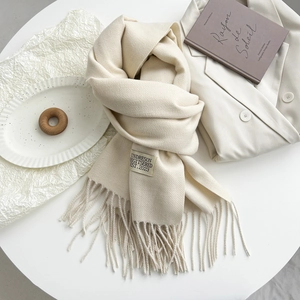 Detail of soft cream cashmere scarf featuring fine fringe and branded woven label