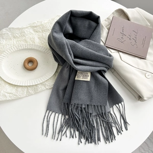 Detail of dark grey scarf with soft fringe and woven brand label on white table