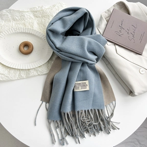 Detail of light blue and beige double-sided scarf with tassels and woven label