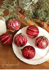 Detailed view of red matte Christmas ball with gold glitter patterns on a white plate