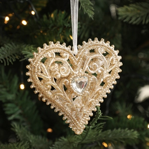 Close-up of golden hollow heart ornament with glitter and jewel on Christmas tree branch