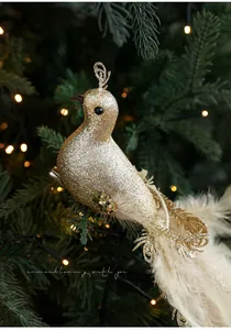 Close-up of golden sequined bird ornament with feathers and metal clip on a Christmas tree
