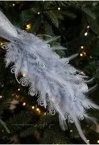 Silver glitter peacock bird ornament with feathers hanging on a Christmas tree branch