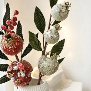 Artificial pomegranate branch with red glitter berries and pearls in a white ceramic vase
