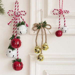 Three assorted metal Christmas bell ornaments with stars and pine hanging on white wall