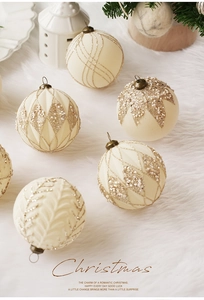 Detalle de bolas de Navidad crema con patrones dorados y perlas sobre piel sintética blanca