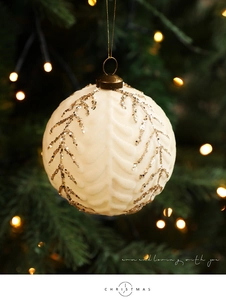 Detalle de bola de Navidad tejida crema con ramas de purpurina dorada en el árbol