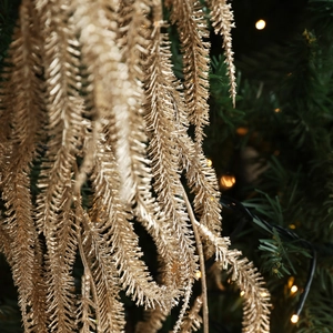 Glittery gold willow leaf branch ornaments hanging on a festive Christmas tree