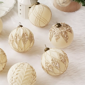 Bolas de Navidad aterciopeladas champán con purpurina dorada sobre fondo de piel blanca