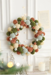 Close-up of colorful flocked ball wreath hanging on wall with warm holiday decorations