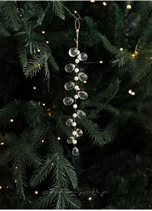 Detail of beaded Christmas ornament with pearls and acrylic ice drops on a glowing tree
