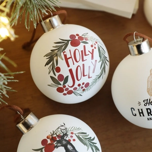 Bola de Navidad blanca mate de 8cm con estampado Holly Jolly, tapa plateada y cordón de cuero