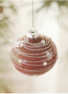 Macro view of a cocoa red Christmas ornament with white glitter swirls and pearls