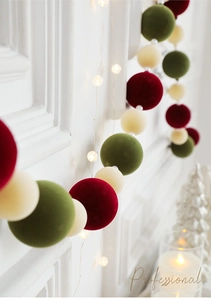 Detail of red and green velvet Christmas balls with warm LED fairy lights on a wall