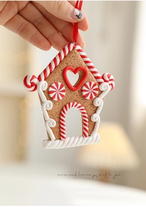 Close-up of a clay gingerbread house ornament with candy cane details and red ribbon
