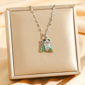 Détail macro du pendentif cigale avec ailes en émail vert et yeux émeraude sur écrin doré