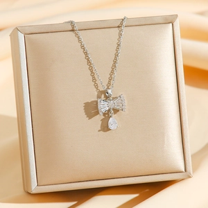 Silver bow necklace with zircon drop pendant on luxury champagne silk background