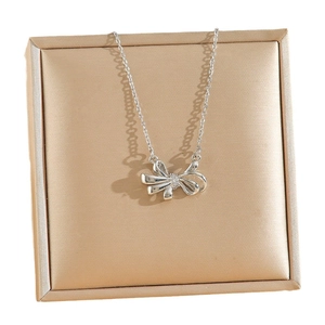 Elegant 18k silver bow pendant necklace with crystal accents on a gold jewelry pad