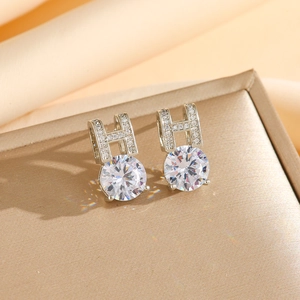 Macro shot of silver letter H earrings with sparkling round zircon studs on champagne silk