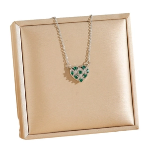 Collier avec pendentif cœur et zircons verts posé sur un coffret à bijoux champagne