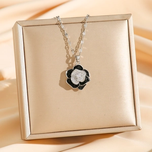Vintage camellia necklace with black enamel and diamond petals on a golden display stand