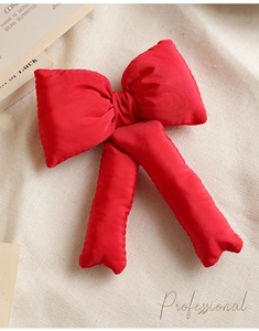 Detail of a plush red fabric Christmas tree topper bow on textured cream cloth