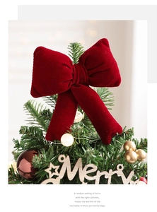 Close-up of a large dark red velvet bow ornament topper on a Christmas tree