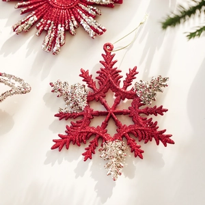 Detail of red glitter snowflake ornament with gold string hanging on festive pine branch