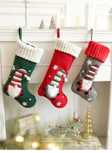 Three plush Christmas stockings with gnome appliques hanging on a festive white fireplace