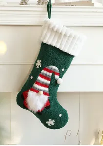Detail of plush green Christmas stocking with gnome embroidery hanging on white fireplace