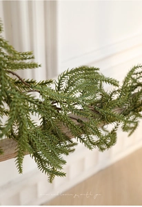 Close-up of realistic faux green pine needle garland on wooden beam for holiday decor