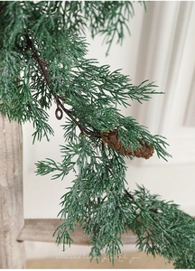 Close-up of artificial pine branch with green needles, brown pinecone and faux snow effect