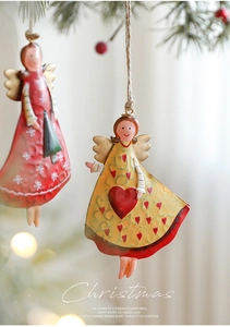 Detailed close-up of retro iron angel ornaments with red heart and gold wings on a pine tree