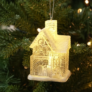 Close-up of glowing transparent Christmas house ornament with snow texture on a tree