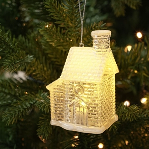 Close-up of glowing LED Christmas house ornament with warm light on a festive tree branch