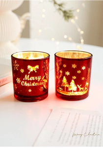 Détail de photophores de Noël en verre rouge avec motifs dorés de rennes et de flocons